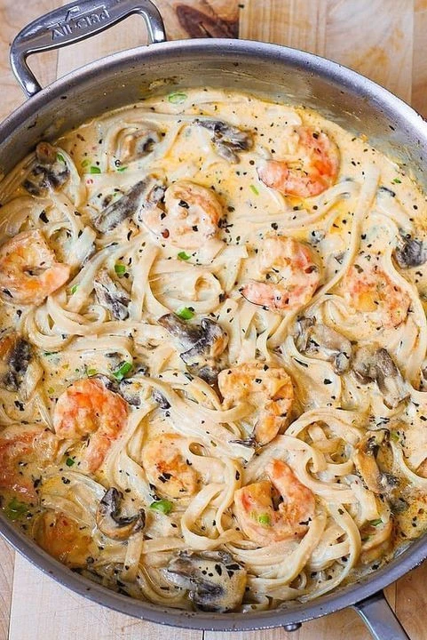 Creamy shrimp pasta with mushrooms in a white sauce garnished with herbs.