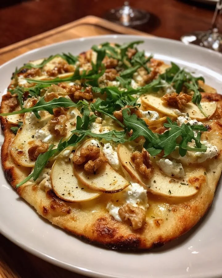 Apple and goat cheese flatbread with walnuts and arugula on a wooden board