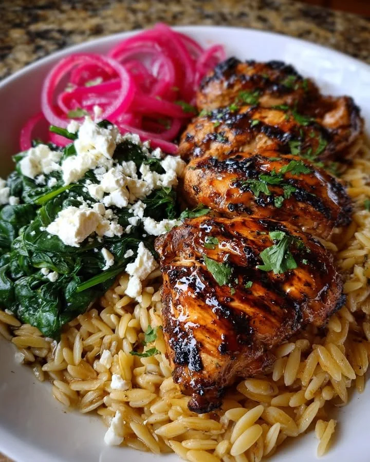 Balsamic glazed chicken served with orzo, feta cheese and sautéed spinach on a plate.