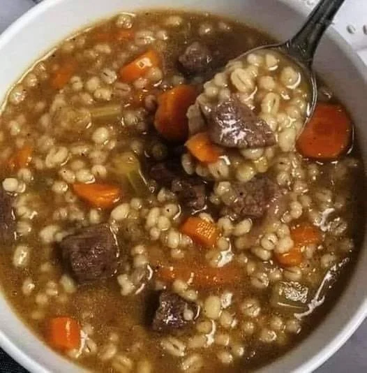 Delicious beef barley soup in a bowl topped with fresh herbs.