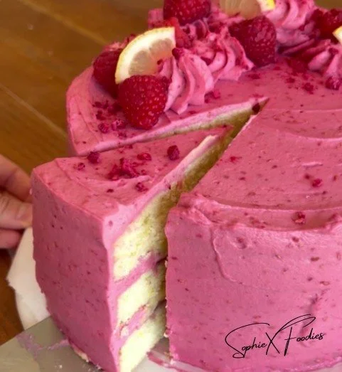 Bright pink raspberry lemon cake topped with fresh raspberries and lemon slices.