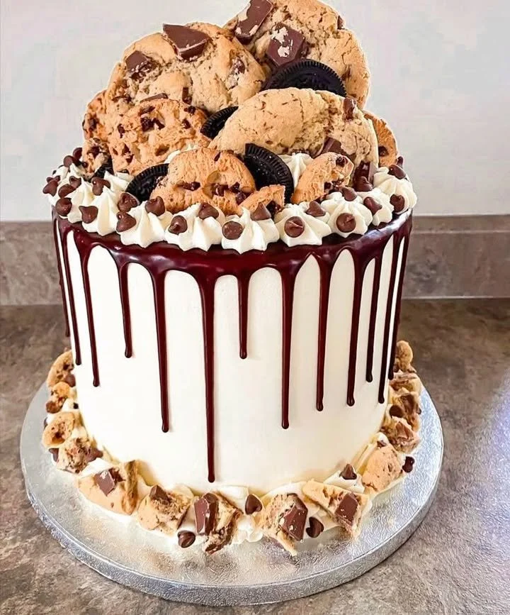 Chocolate chip cookie drip cake topped with chocolate drizzle and cookie pieces.
