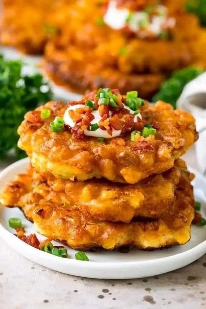 Golden brown corn fritters served on a plate with dipping sauce.