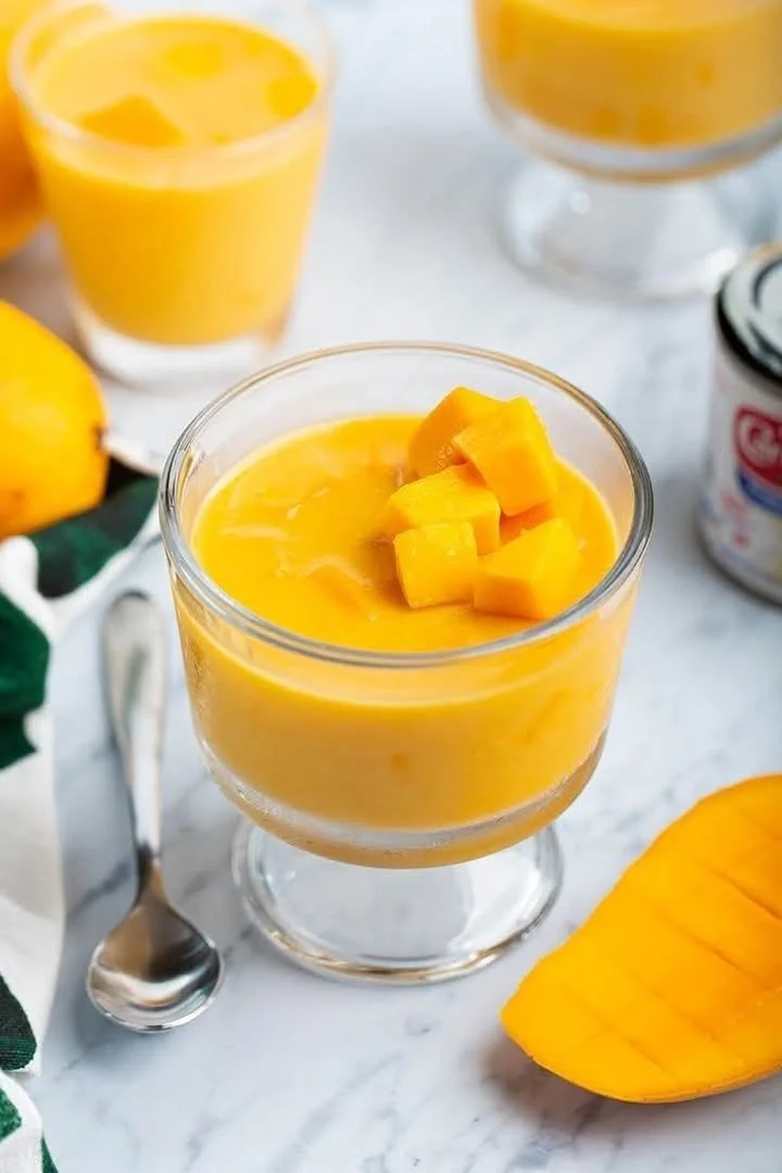 Creamy mango pudding served in a glass bowl with fresh mango slices on top
