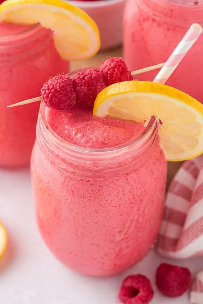 Frozen Raspberry Lemonade served in a glass with fresh raspberries and lemon slices
