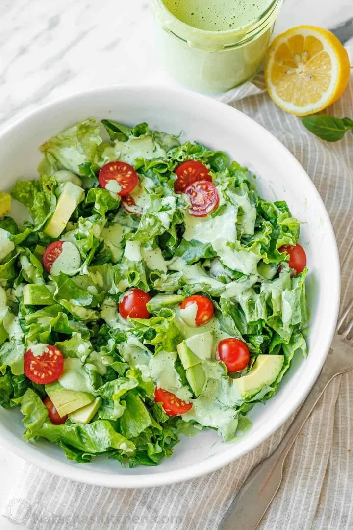 Homemade Green Goddess Dressing in a bowl with fresh herbs and vegetables