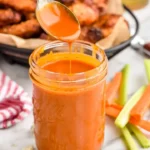 Bottle of homemade buffalo sauce in a bowl with chicken wings