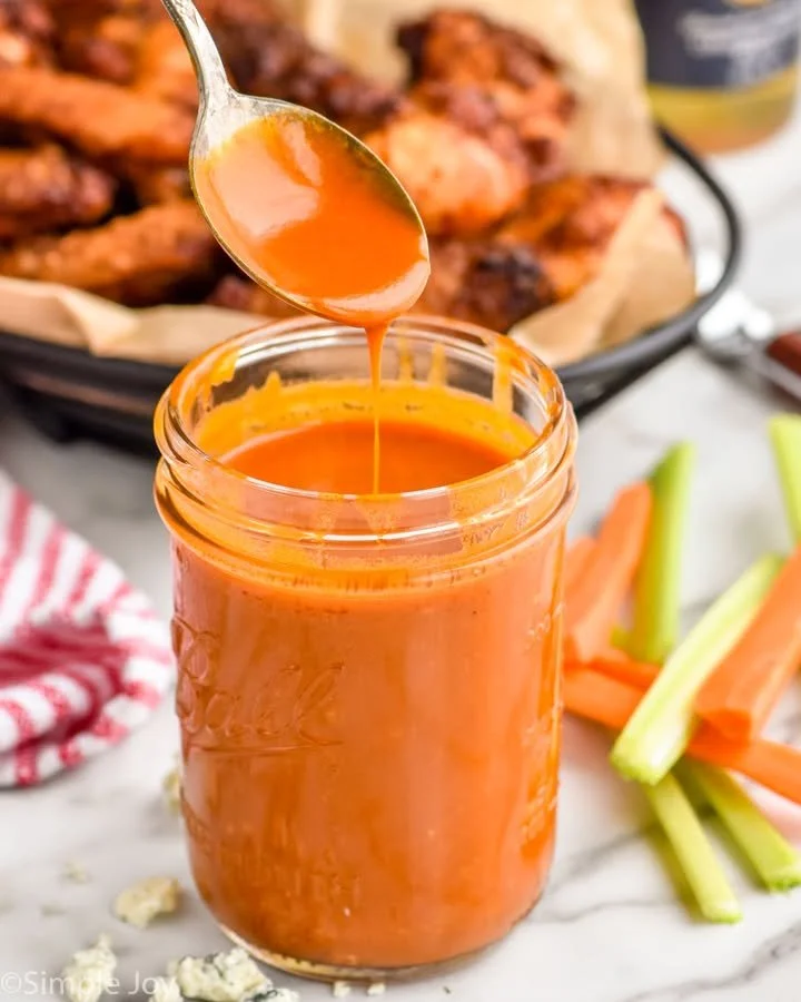 Bottle of homemade buffalo sauce in a bowl with chicken wings