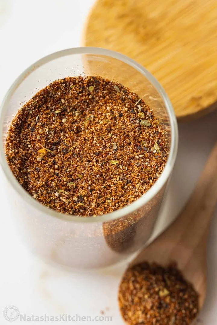 Jar of homemade taco seasoning with spices on a wooden table.