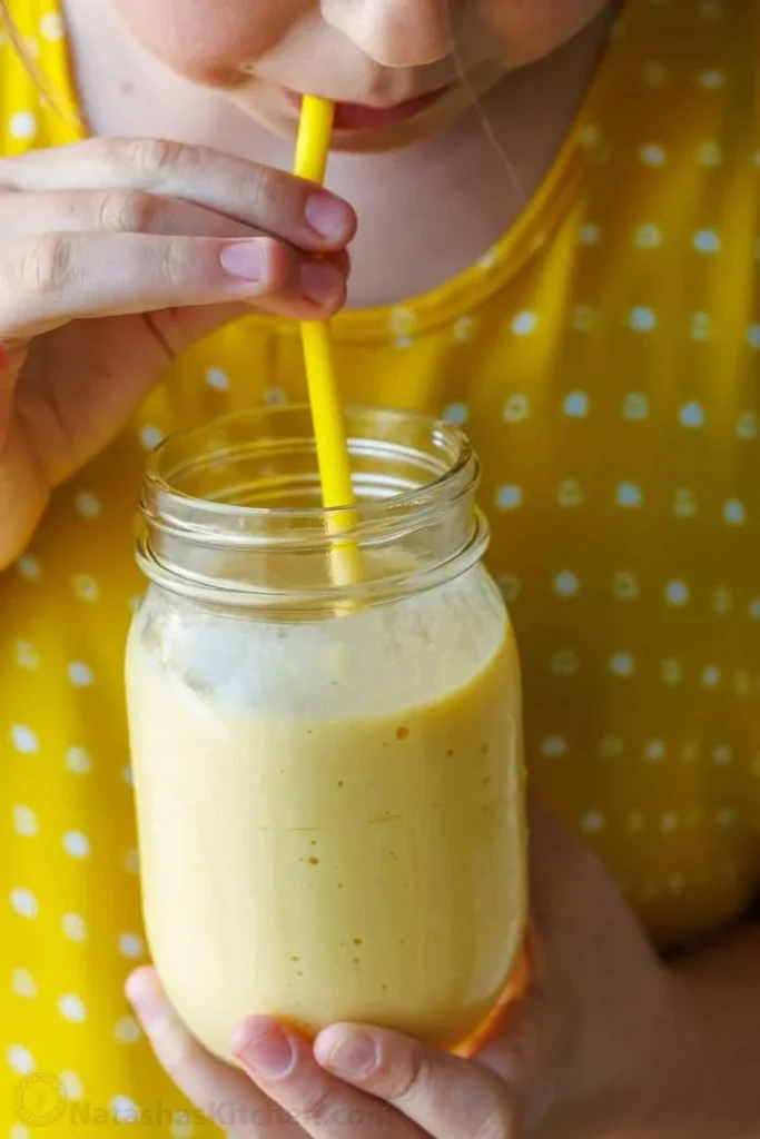 A refreshing mango smoothie served in a glass with a slice of mango on top