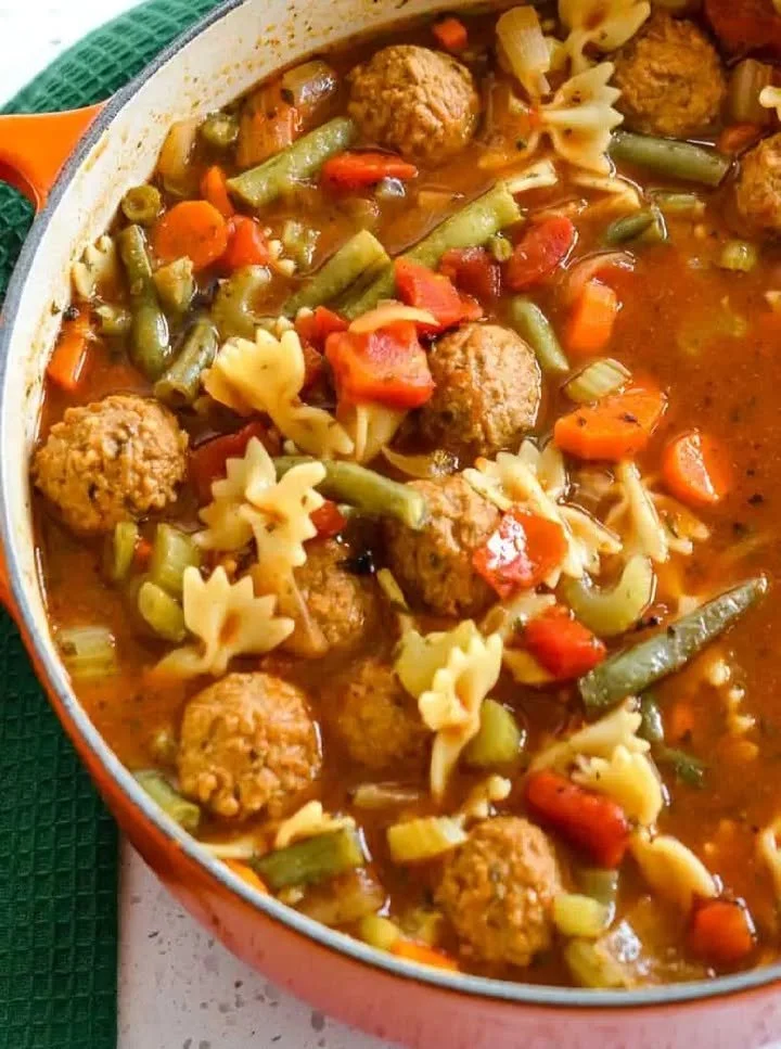 A steaming bowl of delicious Meatball Soup garnished with herbs and spices.