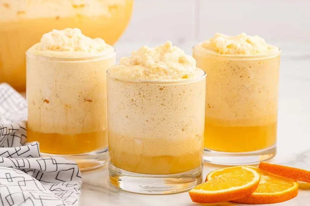 A glass of Orange Dreamsicle Punch with oranges and ice, refreshing summer drink.