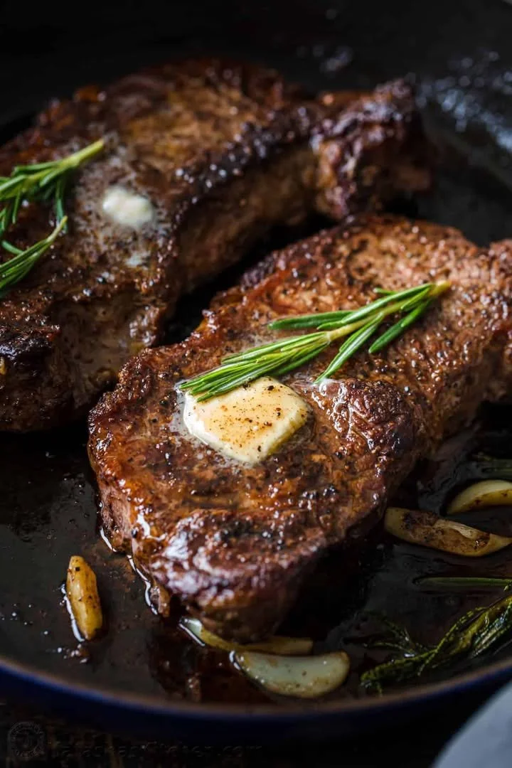 Delicious pan-seared steak on a plate garnished with herbs.