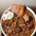 Pinto beans with ham hocks served alongside cornbread on a rustic table.