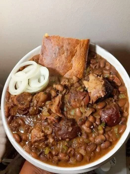 Pinto beans with ham hocks served alongside cornbread on a rustic table.