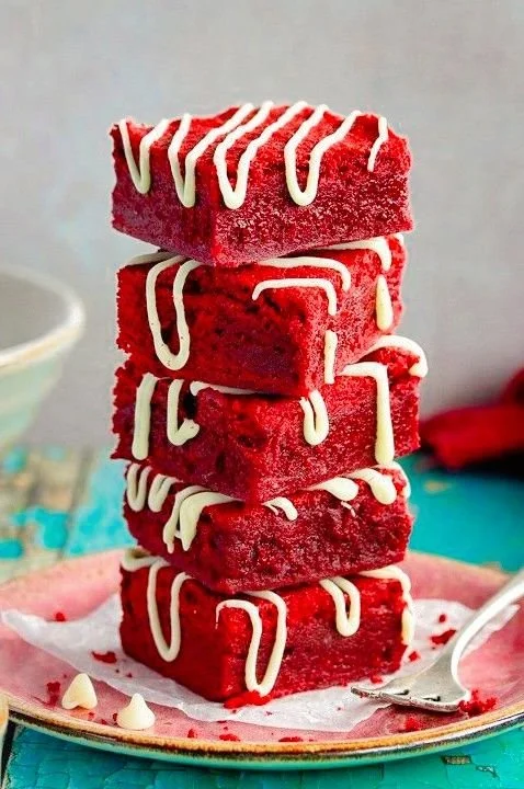 Decadent red velvet brownies topped with a drizzle of white chocolate