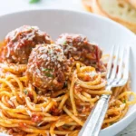 A plate of spaghetti and meatballs topped with fresh parsley and grated cheese.
