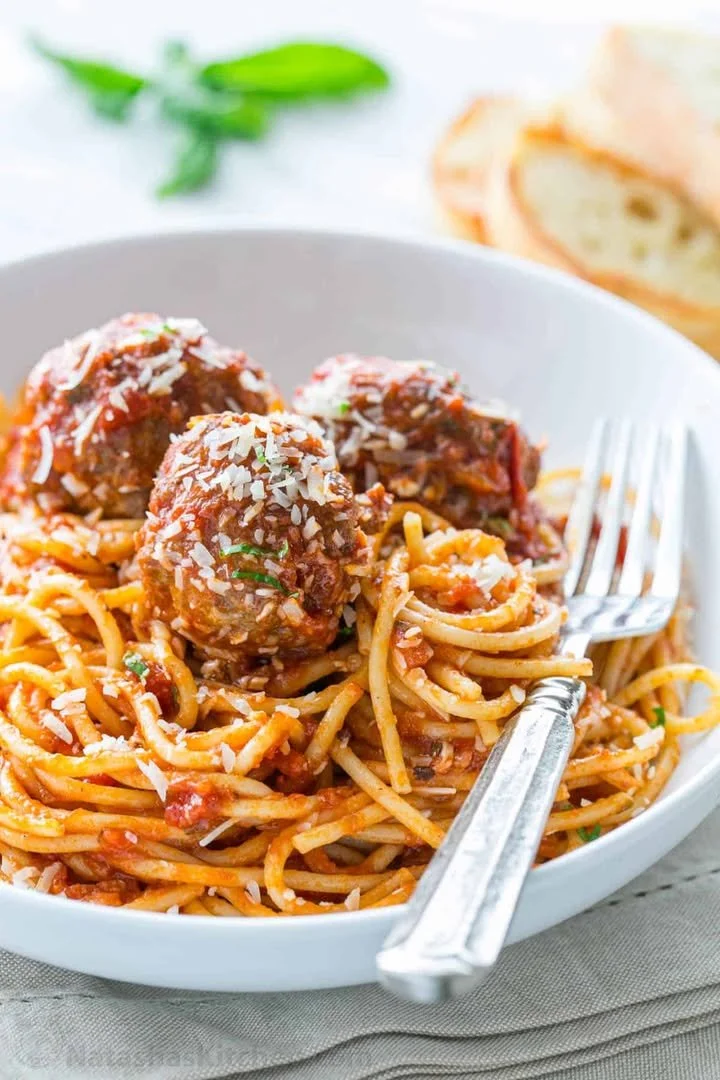 A plate of spaghetti and meatballs topped with fresh parsley and grated cheese.