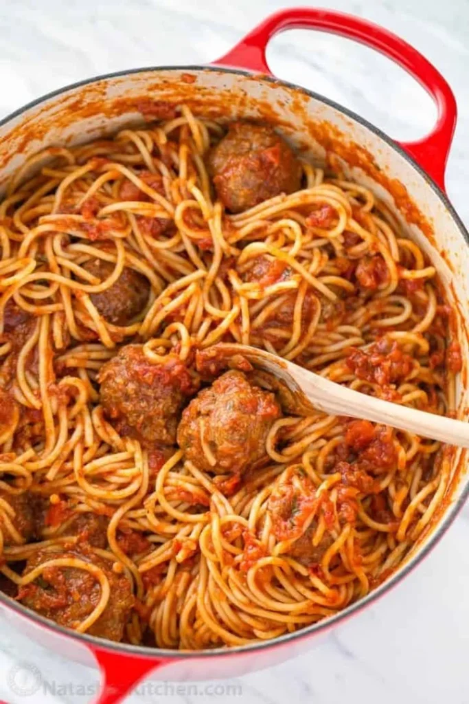Plate of spaghetti meatballs garnished with fresh herbs and Parmesan cheese