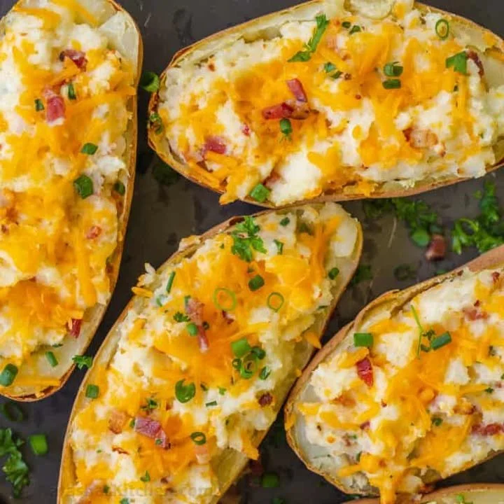 Twice baked potatoes topped with cheese and chives on a plate.