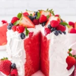 Slice of colorful Watermelon Cake topped with whipped cream and fresh fruits