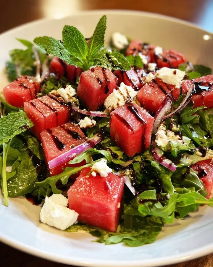 Watermelon feta arugula salad drizzled with balsamic glaze on a plate