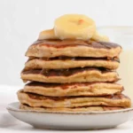 Fluffy banana protein pancakes on a plate, garnished with fresh banana slices.