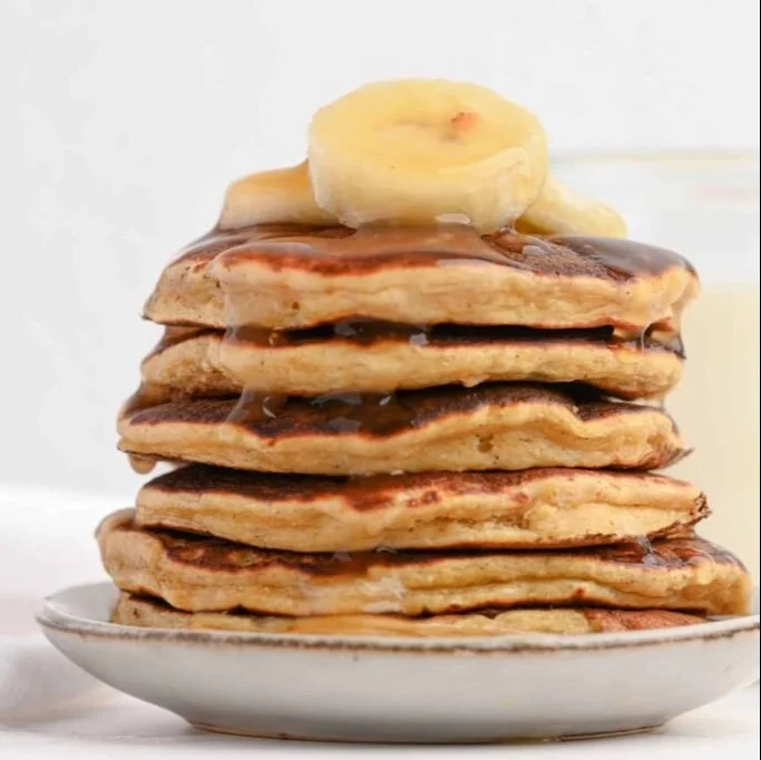 Fluffy banana protein pancakes on a plate, garnished with fresh banana slices.