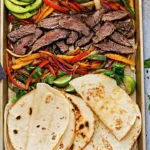 Plate of beef fajitas with colorful veggies and soft tortillas.
