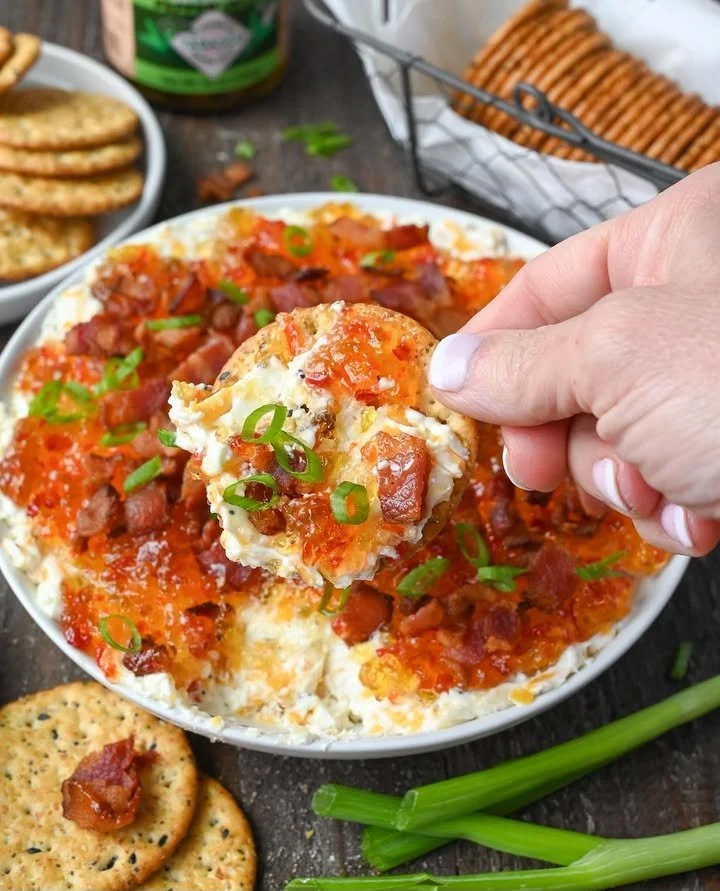 Cream cheese pepper jelly dip served in a bowl with crackers and vegetables.