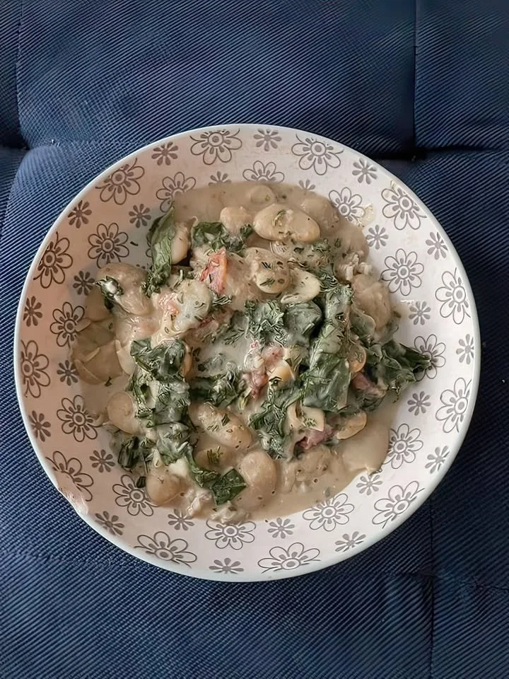 Creamy Tuscan butter beans with spinach in a bowl, garnished with herbs.