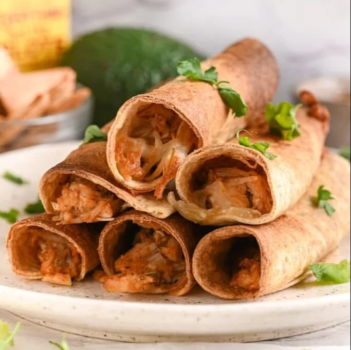 Plate of crispy chicken taquitos served with salsa and guacamole.