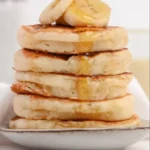 Fluffy Greek yogurt pancakes stacked on a plate with fresh fruit.