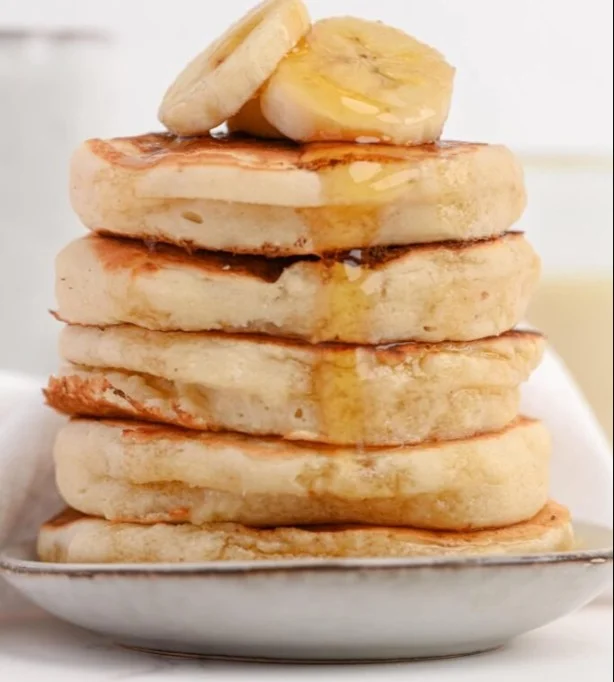 Fluffy Greek yogurt pancakes stacked on a plate with fresh fruit.