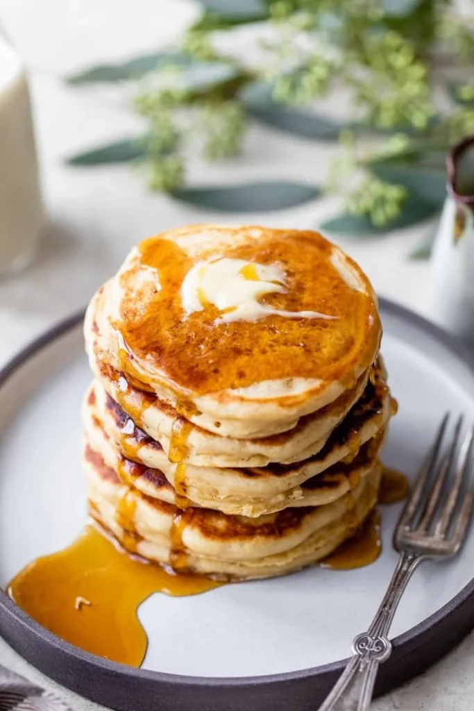 Stack of fluffy pancakes with syrup and berries on a plate