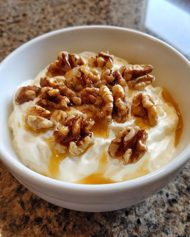 Bowl of Greek yogurt topped with honey and walnuts.