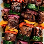 Grilled beef kabobs skewered with colorful peppers and onions on a barbecue grill.