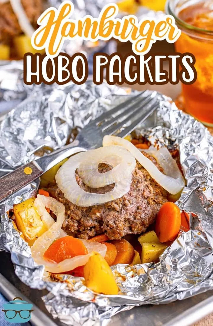 Hamburger hobo packets cooking over a campfire in aluminum foil.