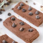 Homemade chocolate protein bars on a wooden surface with chocolate pieces