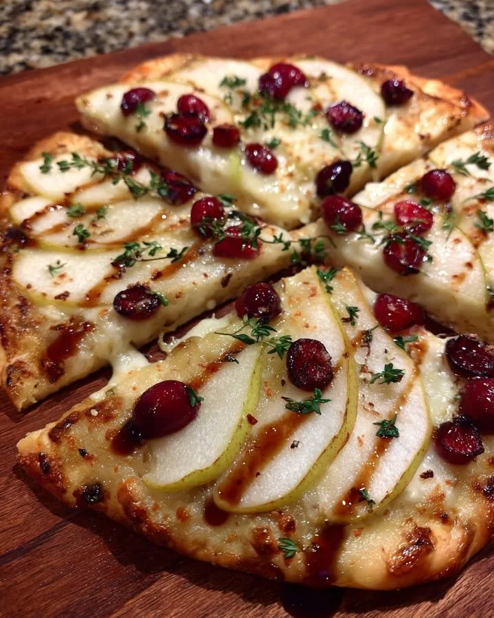 Pear, Brie, and Cranberry Flatbread garnished with thyme on a wooden serving board.