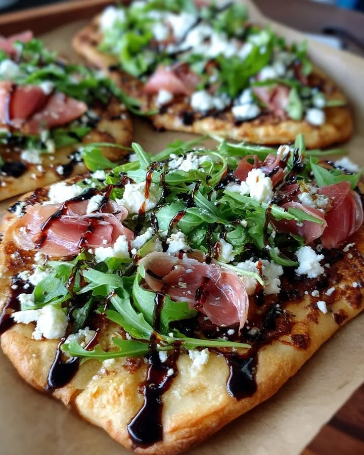Prosciutto fig flatbread topped with arugula and goat cheese on a wooden board.