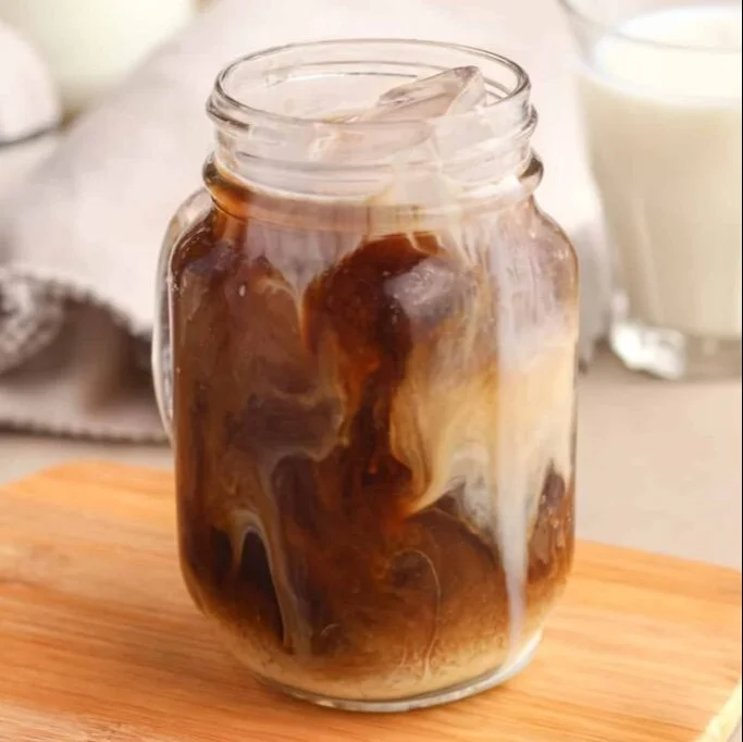 A cup of protein coffee with milk and coffee beans on a table