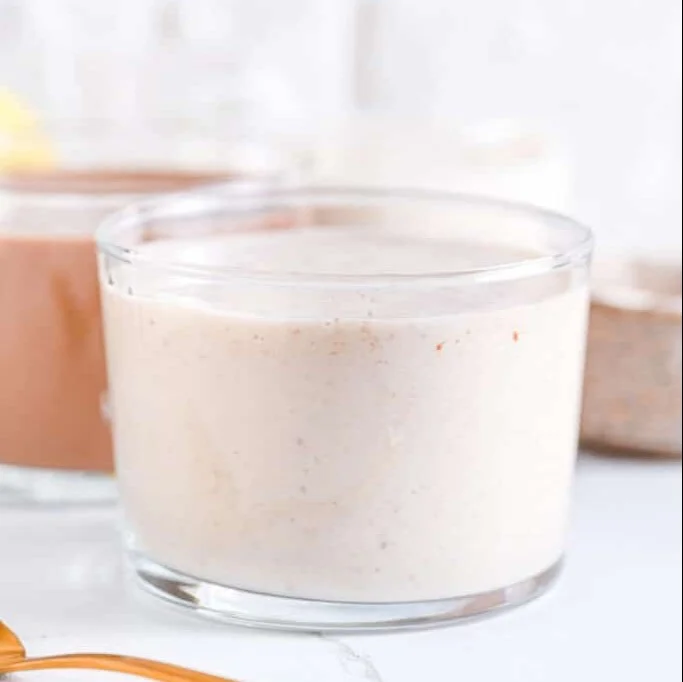 A creamy vanilla protein shake in a glass with a scoop of protein powder