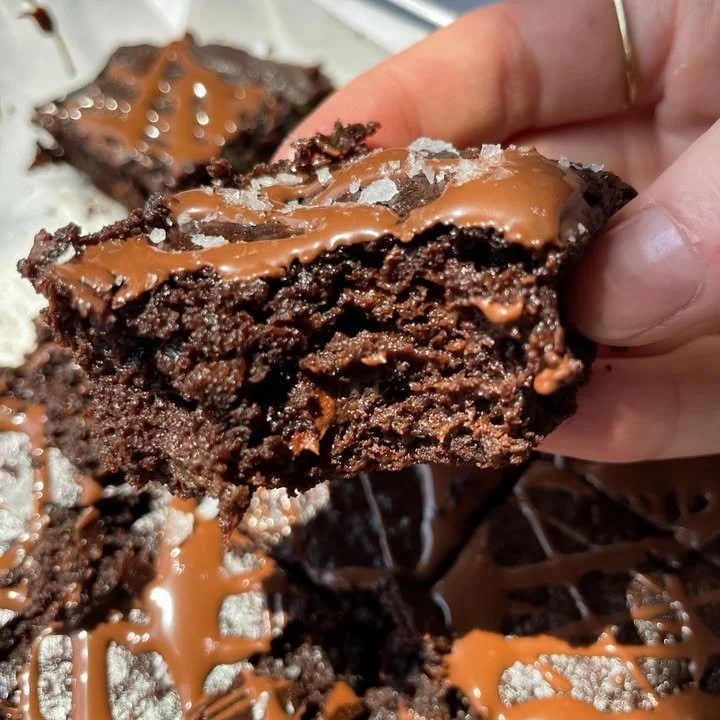 Delicious zucchini brownies topped with flaky sea salt on a wooden table.