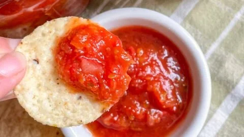 Jar of homemade canned salsa with fresh vegetables and herbs.
