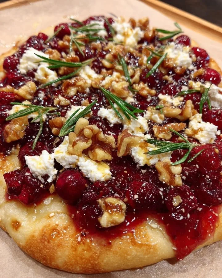Cranberry flatbread topped with goat cheese and hot honey on a wooden cutting board.