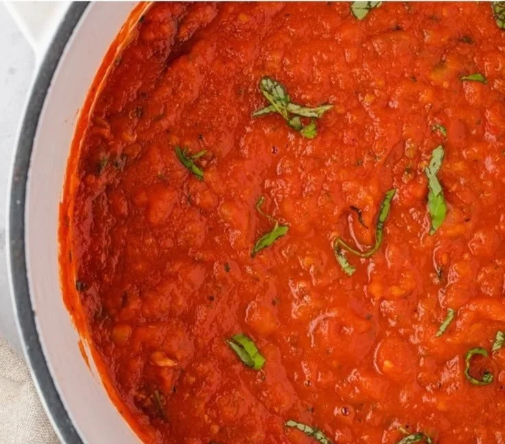 Delicious homemade marinara sauce in a bowl with fresh tomatoes and herbs.