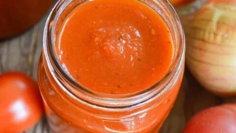 Jar of homemade roasted tomato sauce with fresh tomatoes and basil.