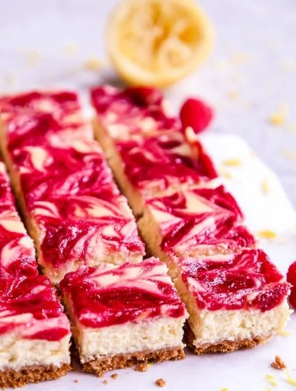 Lemon raspberry cheesecake bars on a white plate with fresh raspberries