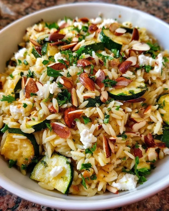 Orzo salad featuring roasted zucchini, feta cheese, and almonds in a colorful bowl.